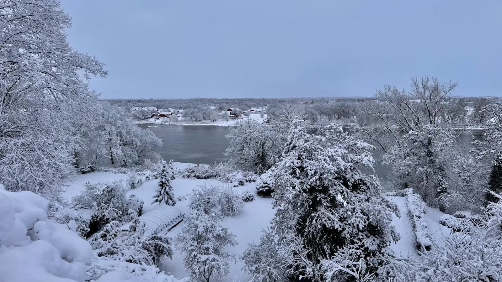 Blick von oben über einen verschneiten Garten auf einen Fluss, am anderen Ufer ein Dorf