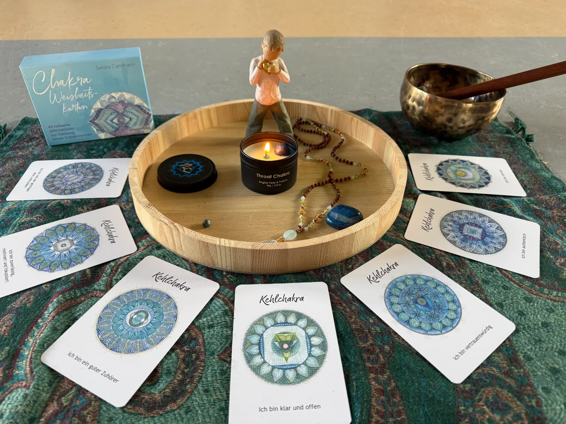 Chakra-Weisheitskarten zum Kehlchakra rund um ein Holztablett mit Kerze und Klangschale