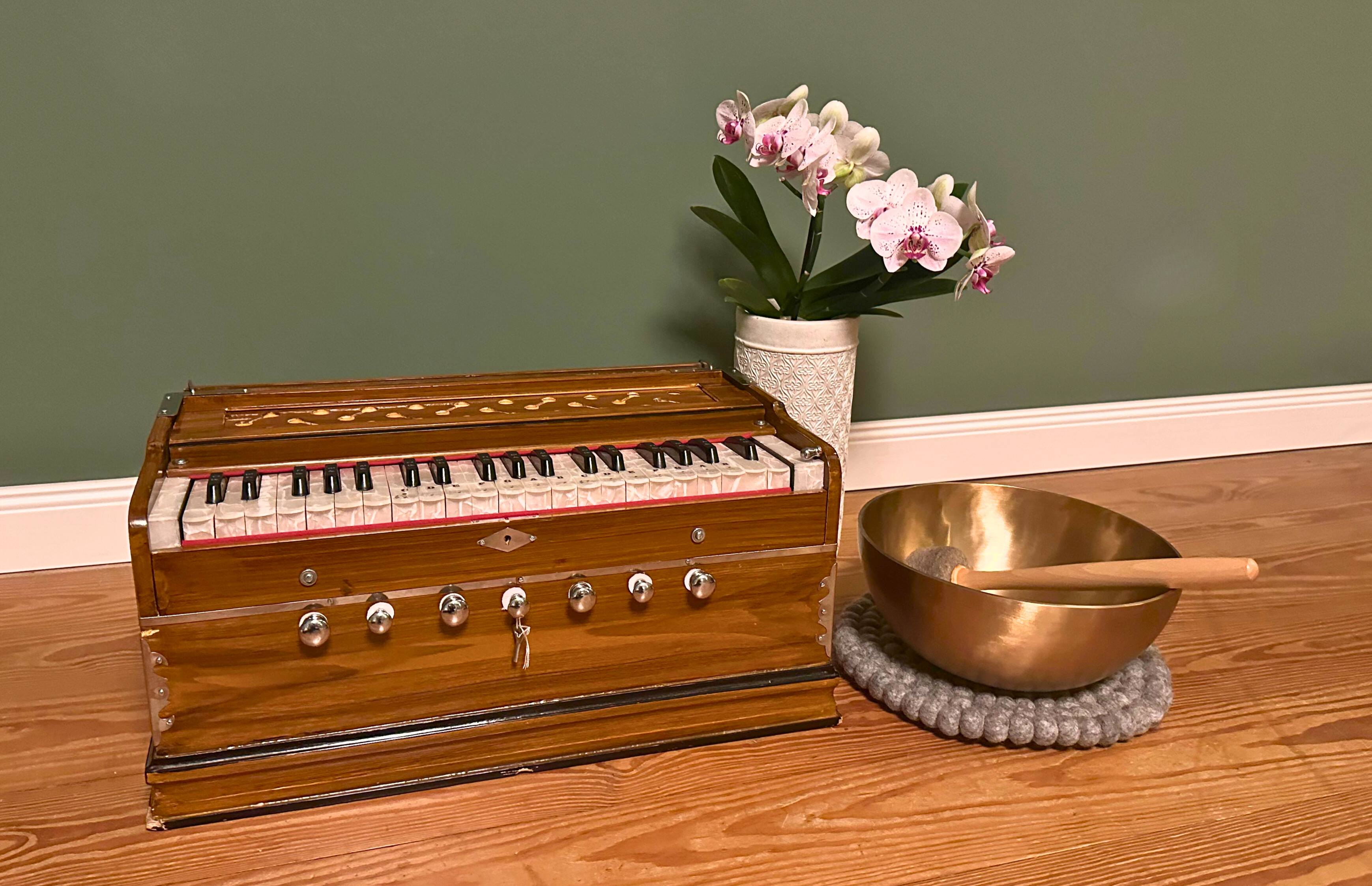 ein Photo mit einem Harmonium, einer Klangschale und einer Orchidee in einem weißen Übertopf